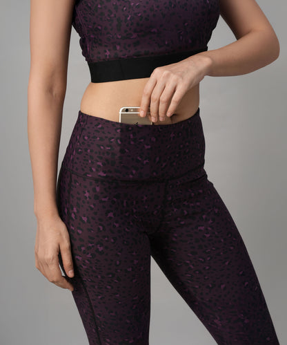 A woman wearing Pink Animal Print Wide Legged Leggings puts her smartphone into the pocket, standing against a gray background.