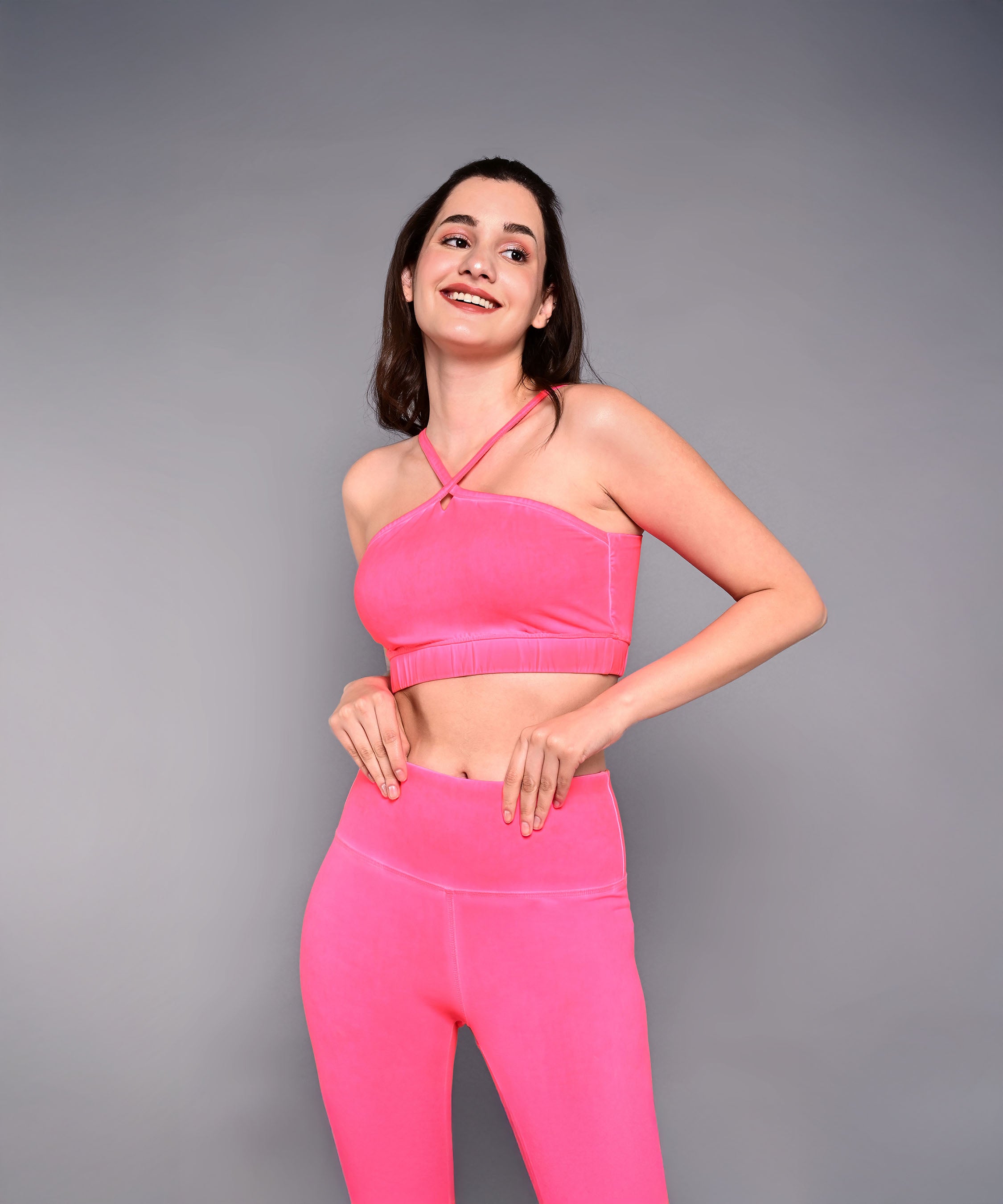 A woman smiles in a Neon Pink Sports Bra made from skin-friendly cotton lycra, standing against a plain gray background.