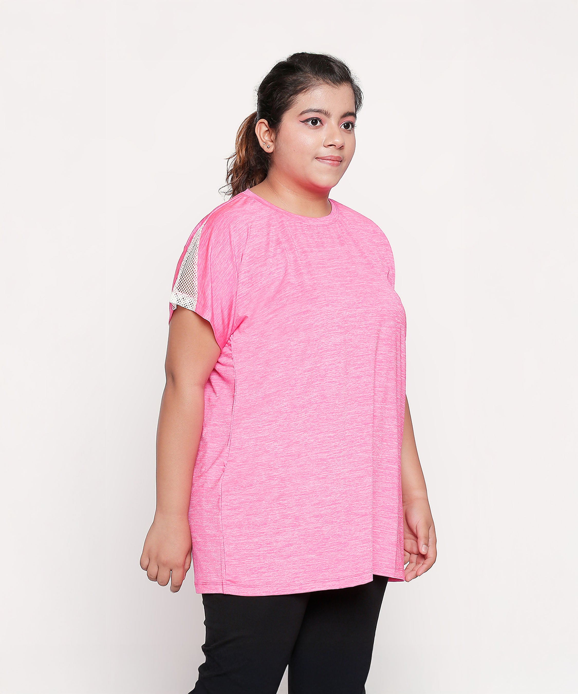 Woman wears the Nova Sports Tee—a loose pink sports top with mesh sleeve detail—standing and looking to the side against a white background; an effortless addition to your workout wardrobe.