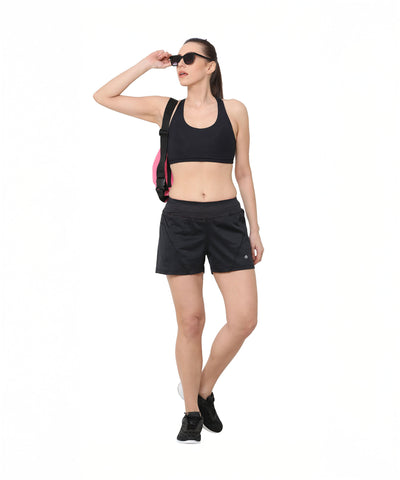 A woman wearing Black Shorts and sunglasses, carrying a pink bag, stands against a white background.