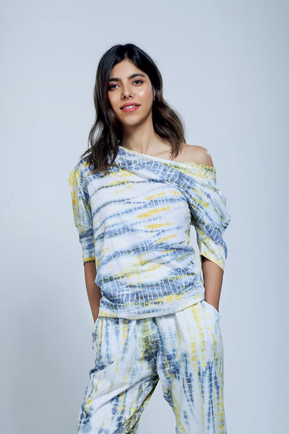 Woman wearing a yellow and grey organic cotton one side off-shoulder top with matching yoga pants, standing and smiling.