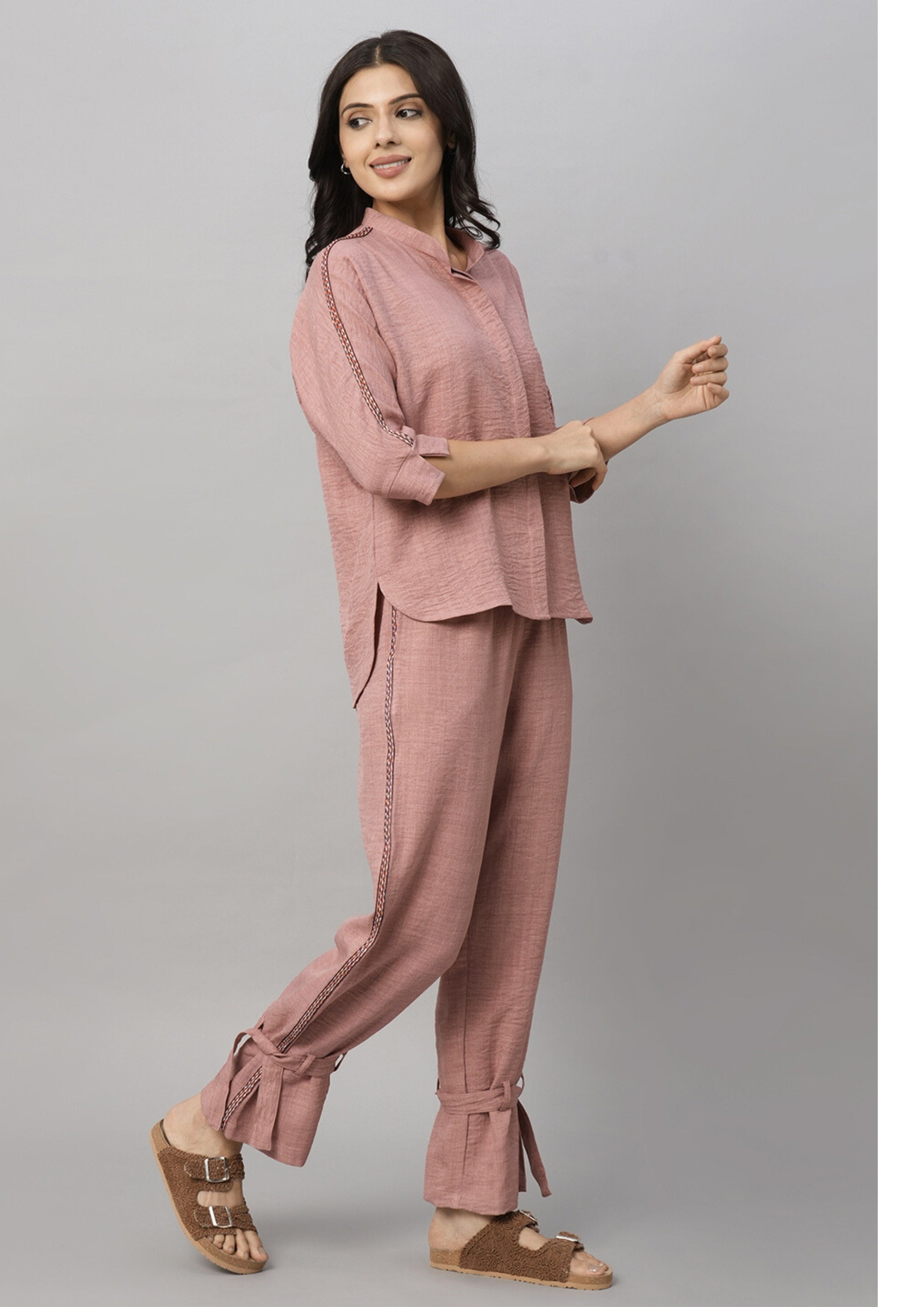 Woman wearing the Vintage Pink Loose Shirt and Tie Up Pant Cord Set with sandals, standing sideways and smiling against a gray background.