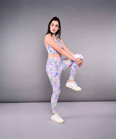 Woman in colorful activewear stands on one leg, holding her knee to her chest, showcasing Multicolour Neon Leggings against a gray background.