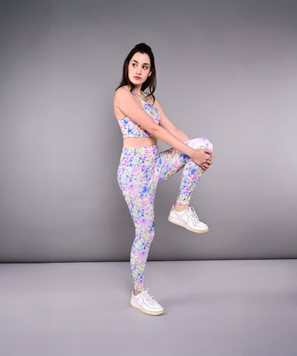 Woman in colorful activewear stands on one leg, holding her knee to her chest, showcasing Multicolour Neon Leggings against a gray background.