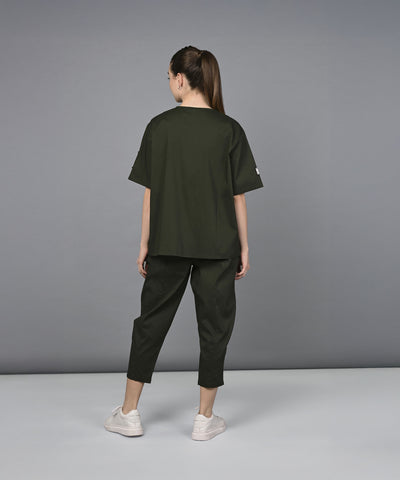 A woman wearing the Military Green Open Jacket & Yoga Pants with Bustiere set and white sneakers stands facing away against a plain gray background.
