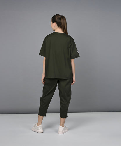 A woman wearing the Military Green Open Jacket & Yoga Pants with Bustiere set and white sneakers stands facing away against a plain gray background.