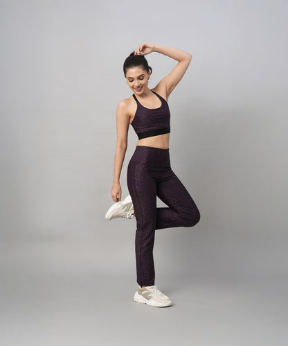 A woman wearing a Pink Animal Print Sports Bra poses on one leg against a plain grey background, smiling and looking down.
