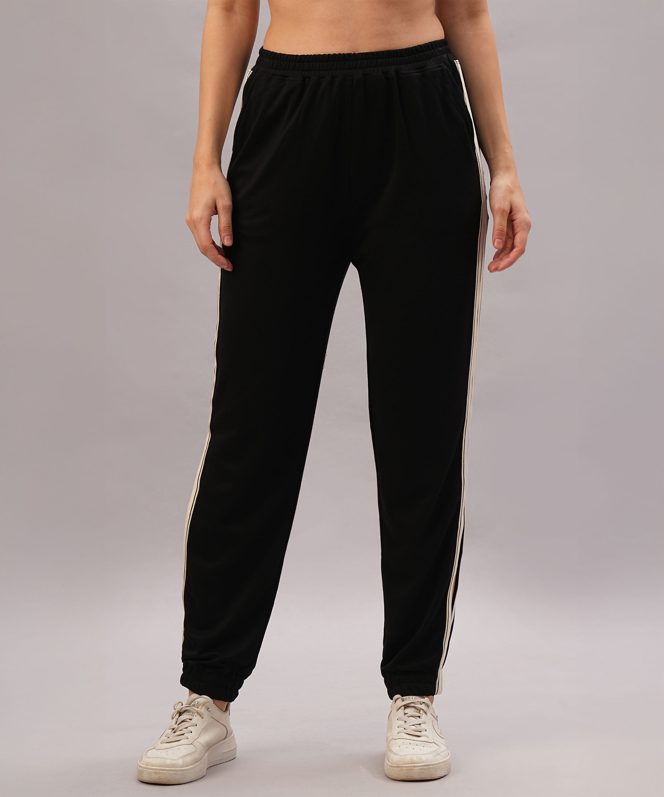 A person models the Black Co-Ord Set made from soft cotton lycra, featuring black track pants with white side stripes, paired with white sneakers against a plain background.