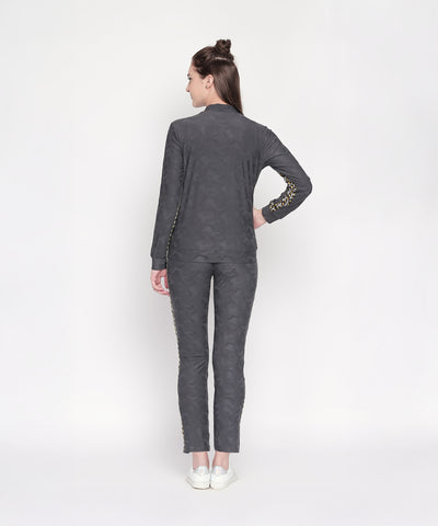 Woman in a matching gray outfit, featuring an Active Wear Printed Jacket in Grey and white shoes, stands with her back to the camera against a white background.