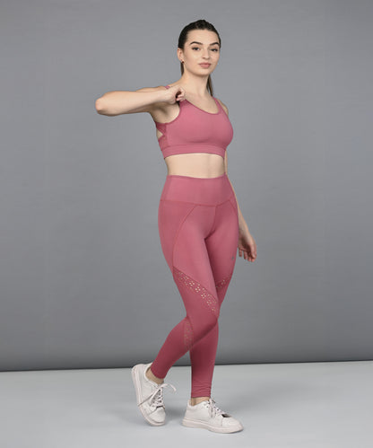 A woman poses confidently against a gray background in the Peony Pink Netted Top paired with white sneakers.