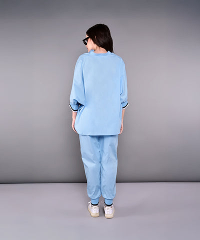 Woman wearing the Denim Accented Set—loose 100% cotton batwing sleeve shirt and joggers—with white sneakers, standing with her back to the camera against a gray backdrop.
