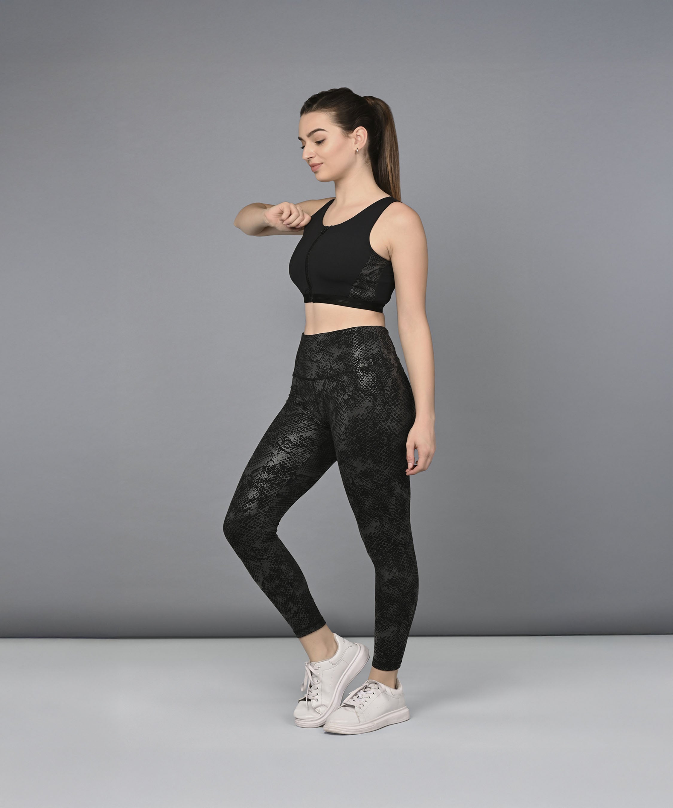 A woman models the Zipped Sports Bra & Metallic Legging, standing sideways against a plain gray background.