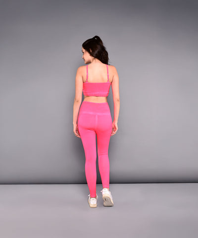A woman models the Neon Pink Sports Bra, made from skin-friendly cotton lycra, standing with her back to the camera against a plain gray background to highlight its vibrant color and comfortable fit.