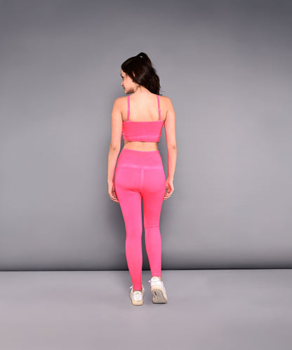 A woman models the Neon Pink Sports Bra, made from skin-friendly cotton lycra, standing with her back to the camera against a plain gray background to highlight its vibrant color and comfortable fit.