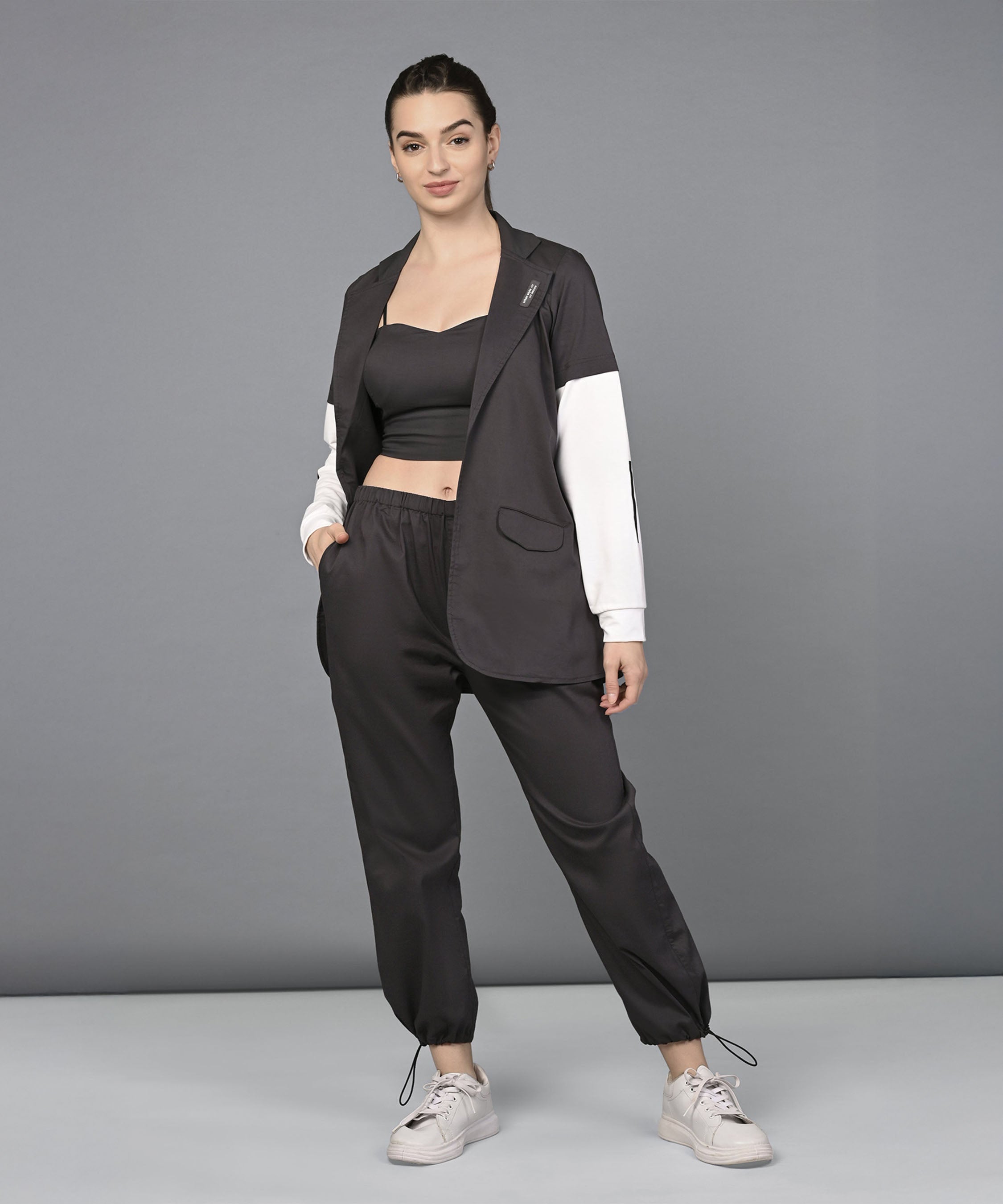 Woman smiling in the Athleisure Blazer Tracks Two Piece Co-ord set: a black crop top and parachute pants paired with a black blazer featuring white sleeves.