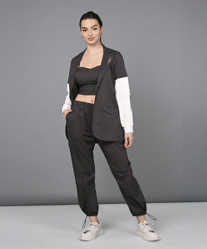 Woman smiling in the Athleisure Blazer Tracks Two Piece Co-ord set: a black crop top and parachute pants paired with a black blazer featuring white sleeves.