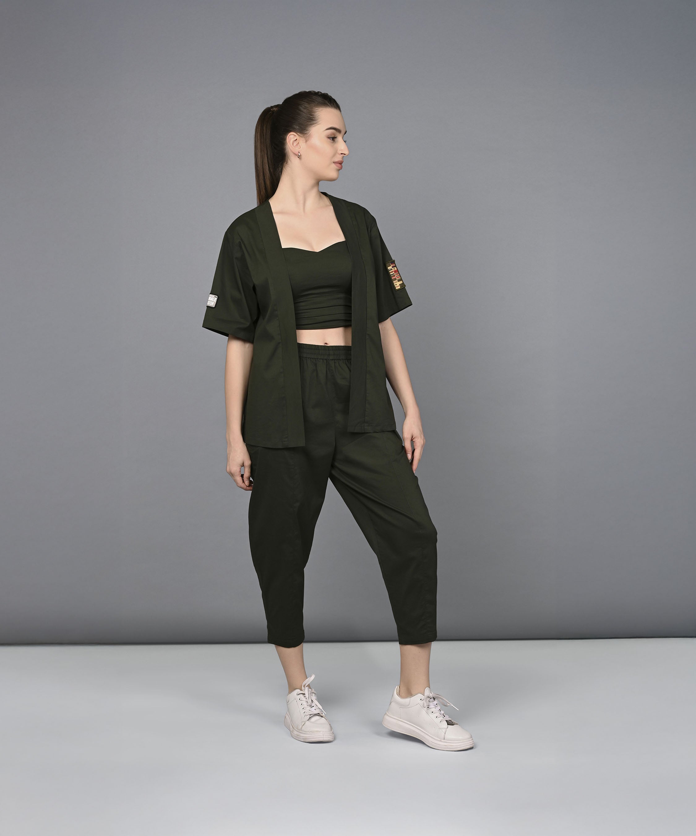 A woman wearing the Military Green Open Jacket & Yoga Pants with Bustiere set stands against a plain gray background, looking to the left.