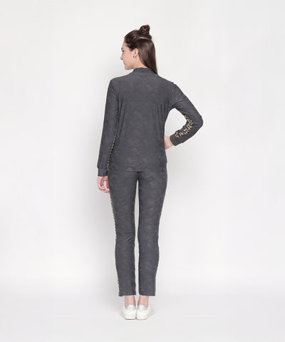 Woman stands with her back to the camera, highlighting chic athleisure style in Self Printed Grey TrackPants and white sneakers against a plain background.