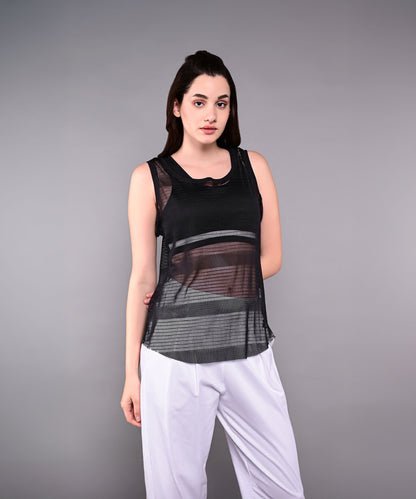 A woman stands against a plain gray background wearing the Tuna Active Black Netted Tank Top paired with white pants.