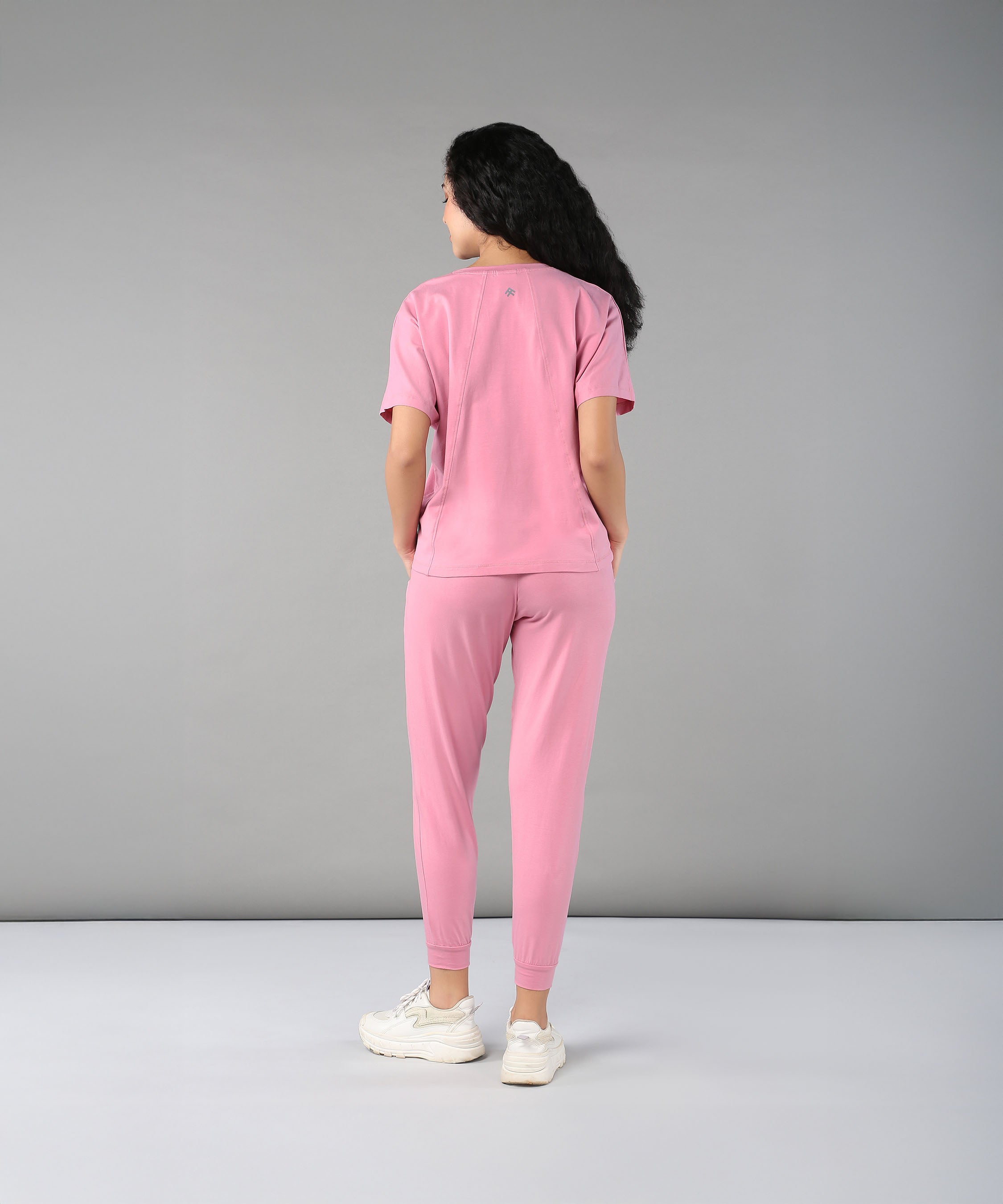 Person wears the Flamingo Pink Chic Ensemble—featuring a buttery soft racer back top and joggers in cotton lycra—while facing away against a plain gray background.