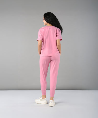 Person wears the Flamingo Pink Chic Ensemble—featuring a buttery soft racer back top and joggers in cotton lycra—while facing away against a plain gray background.