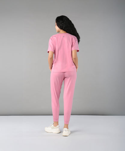 Person wears the Flamingo Pink Chic Ensemble—featuring a buttery soft racer back top and joggers in cotton lycra—while facing away against a plain gray background.
