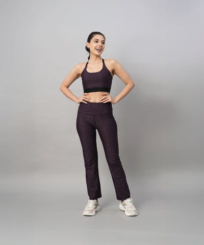 A woman stands smiling against a gray background, wearing stylish activewear: Pink Animal Print Wide Legged Leggings paired with a purple top and white sneakers.