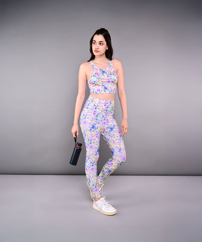 A woman in a colorful workout outfit, featuring Multicolour Neon Leggings and holding a water bottle, stands against a plain gray background.