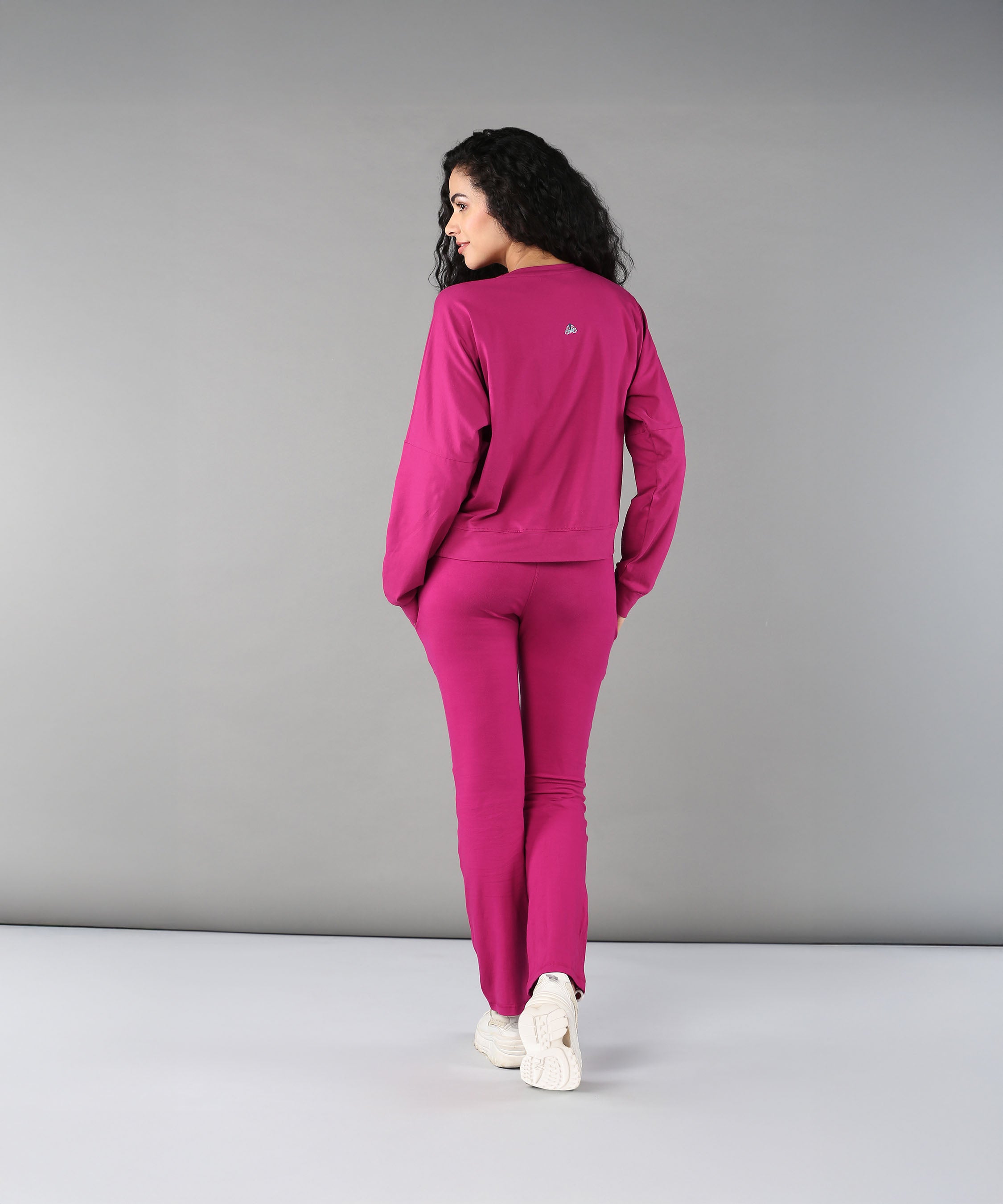 A woman wearing the Deep Pink Comfort Duo set and white sneakers stands facing away against a plain gray background.