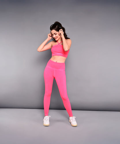 A woman in a Neon Pink Sports Bra made from skin-friendly cotton lycra and white sneakers poses playfully against a plain gray background.