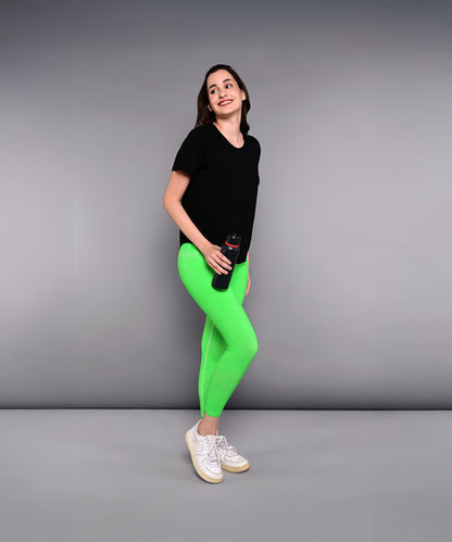 Woman in a 'Pilates Has Your Back' printed tee and bright green leggings holding a water bottle, standing against a gray background.