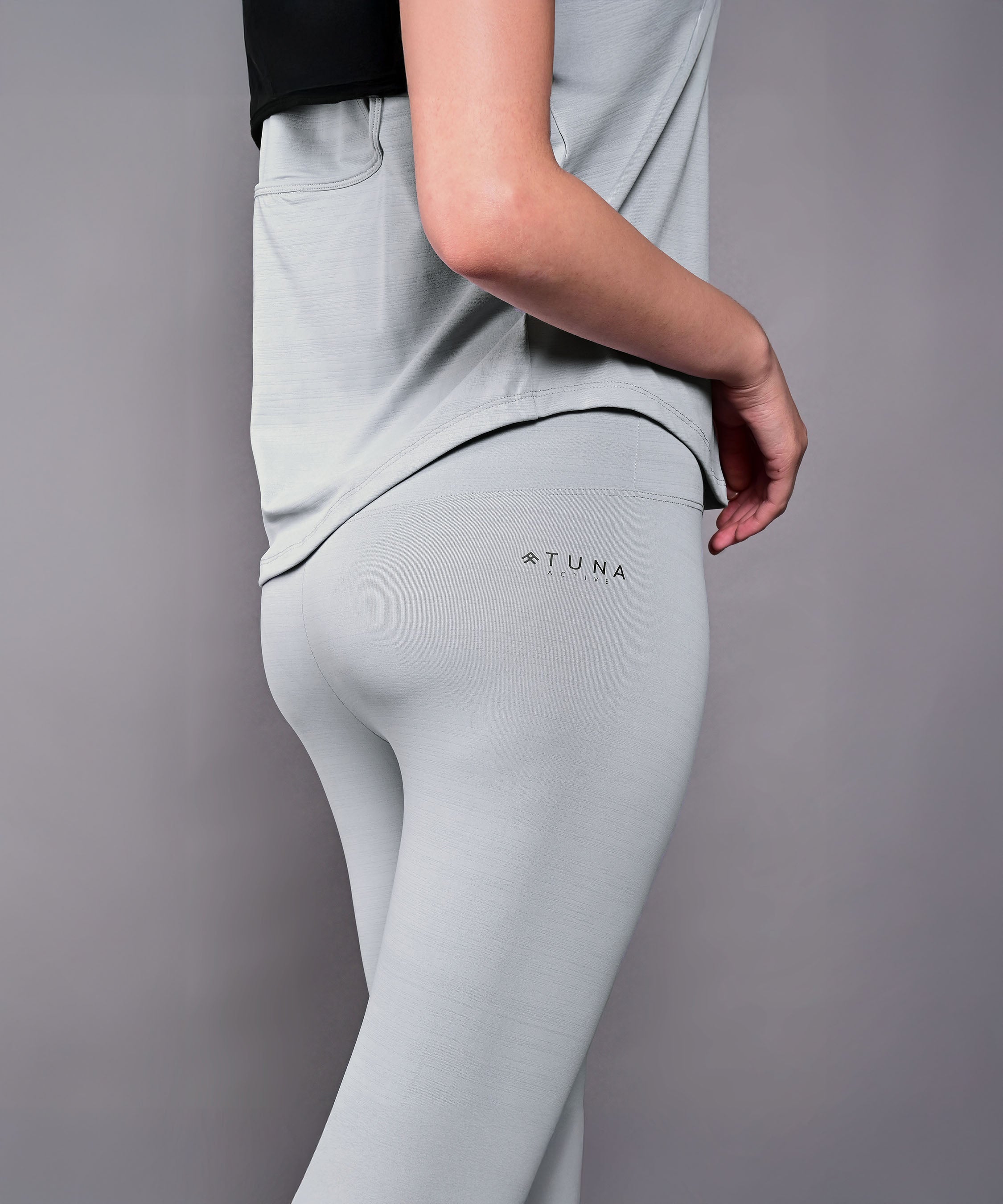 Model in the Dynamic Grey Performance Set, featuring athletic leggings and a grey racerback top, poses sideways against a plain background.