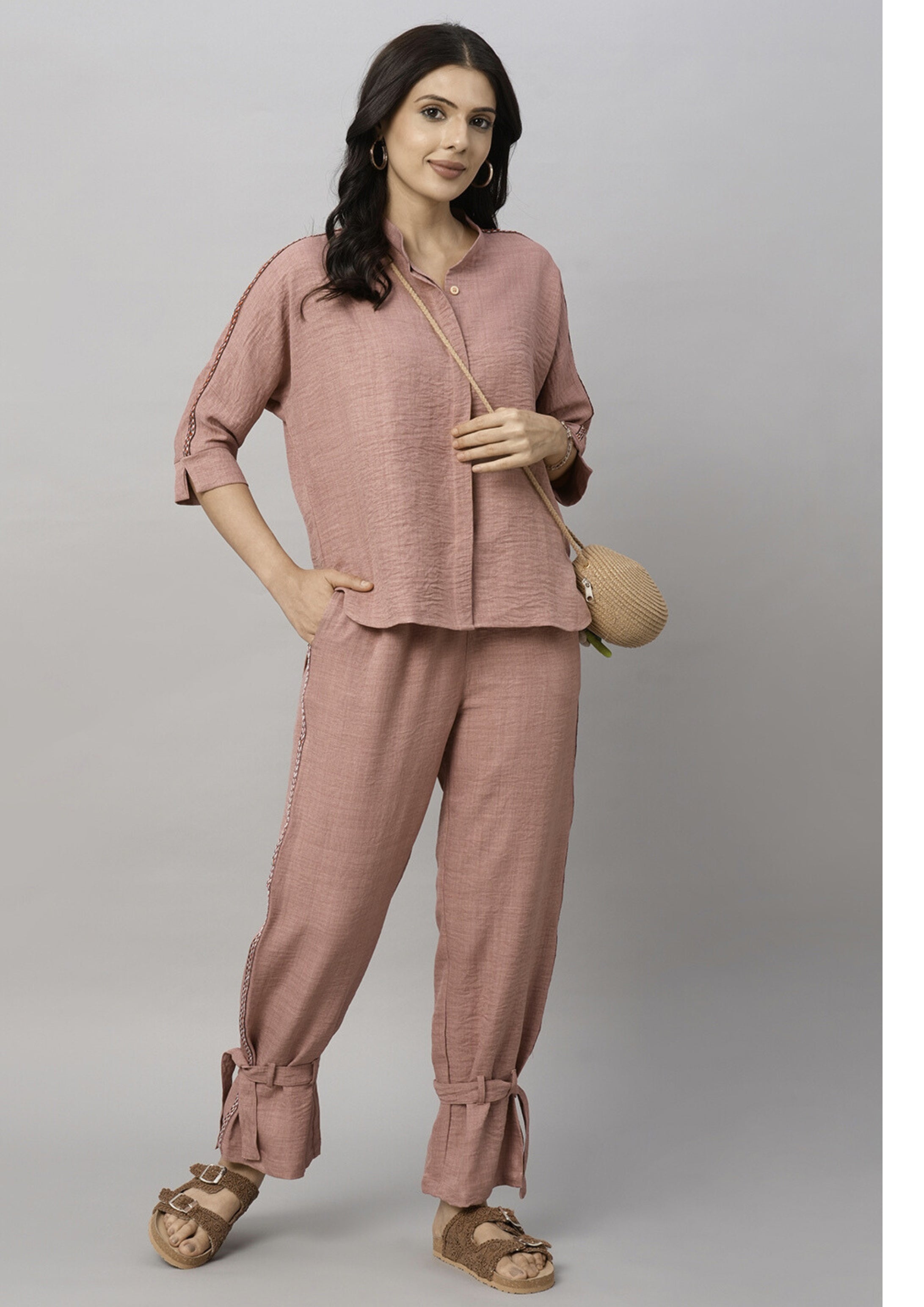 Woman in the Vintage Pink Loose Shirt and Tie Up Pant Cord Set—a 100% cotton outfit styled with brown sandals, hoop earrings, and a small woven crossbody bag.