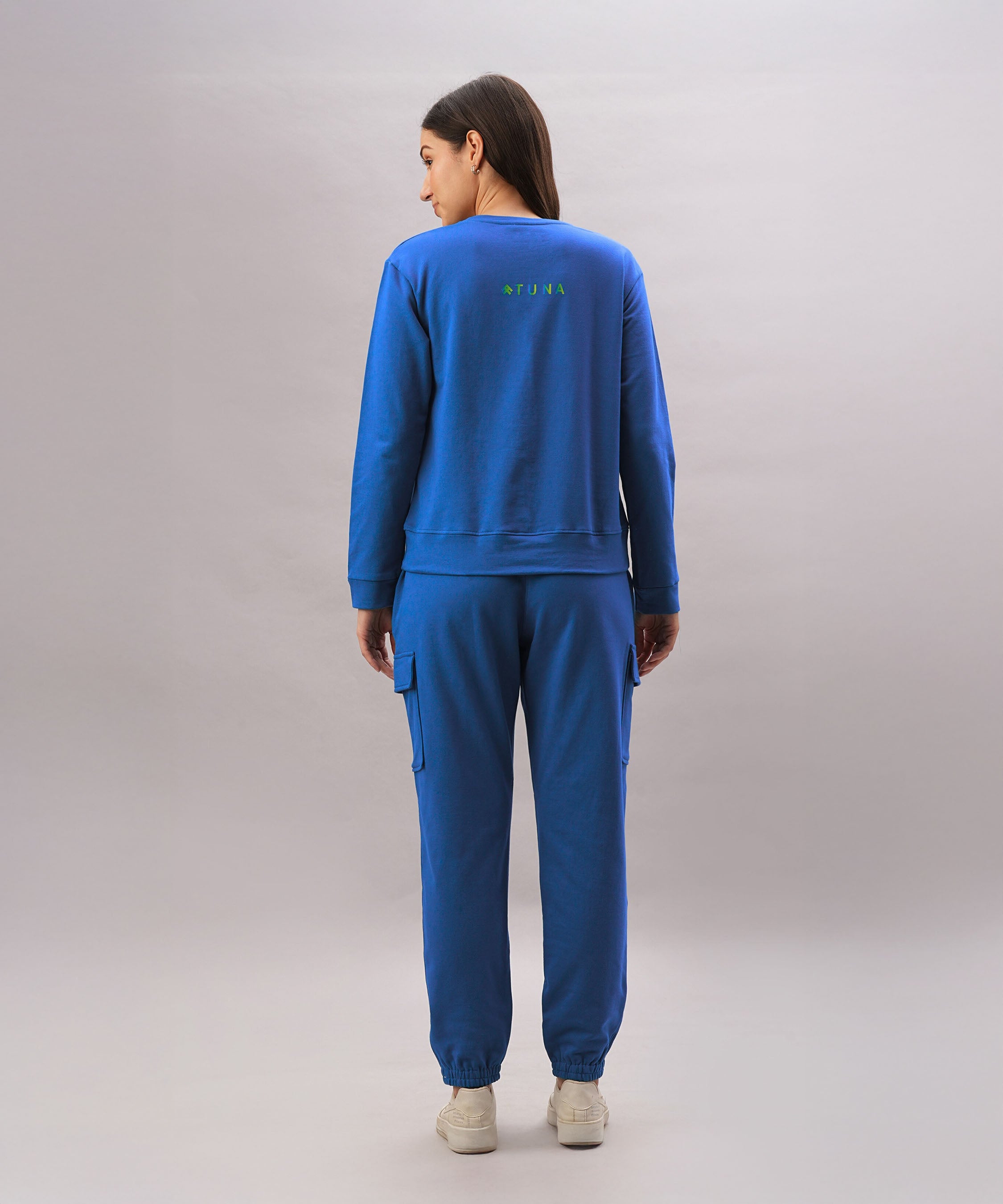 A woman wears the Soft Royal Blue Trackset with cargo-style joggers, standing with her back to the camera against a plain backdrop.