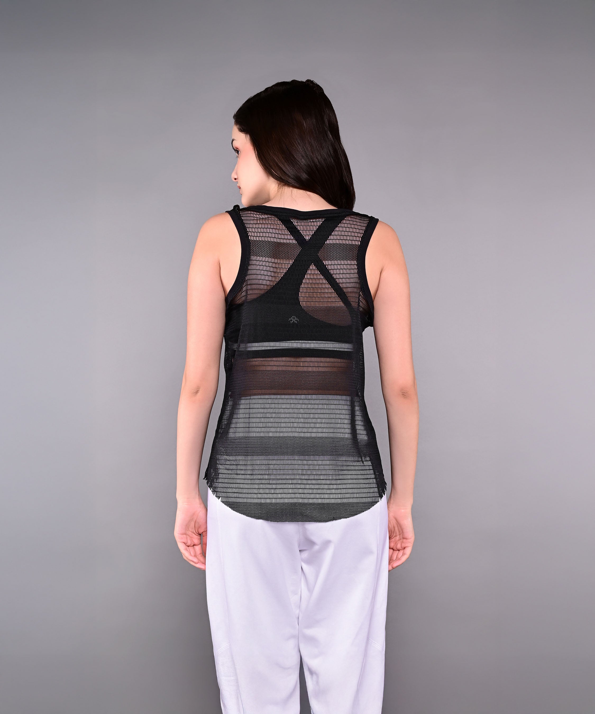 Woman wearing the Tuna Active Black Netted Tank Top and white pants, facing away from the camera against a gray background.
