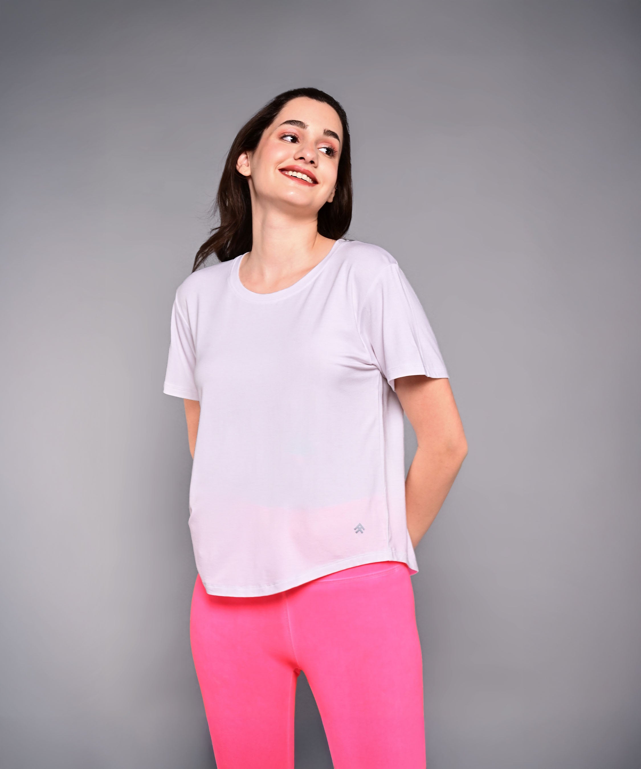 Woman wears the 'Pilates Has Your Back' Printed Tee in light purple with bright pink pants, smiling against a plain gray background.