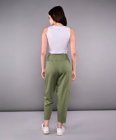 Woman stands with her back to the camera, wearing a White Twisted Crop Top, green pants, and white sneakers.