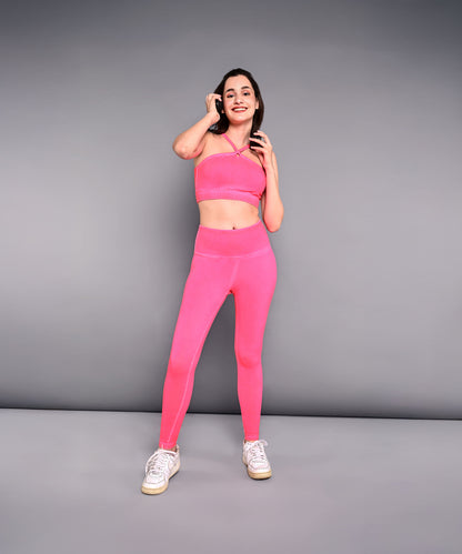 A smiling woman wears the Neon Pink Sports Bra, made from skin-friendly cotton lycra, and poses against a gray wall while holding her hair.