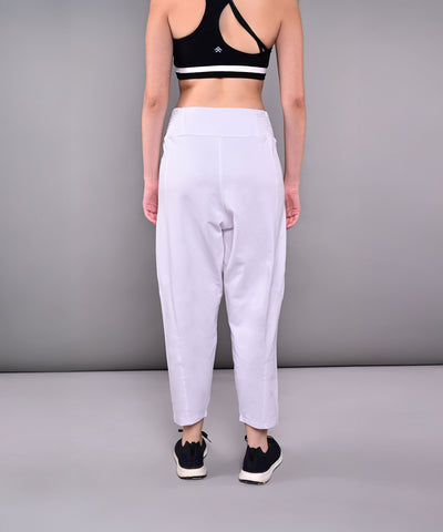 A woman stands with her back to the camera against a gray backdrop, wearing a black sports bra and Pleated Yoga Pant With Smocked Waistband in white cotton.