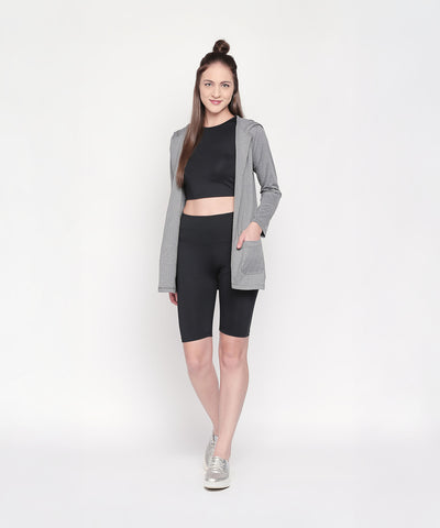 A woman stands and smiles on a white background, wearing a gray hooded jacket, black crop top, and Black Biker/Cycling Shorts featuring a high-rise waistband.