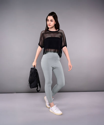 Woman in a Tuna Active Black Netted Top with sheer sporty fabric, holding a black backpack against a plain gray background.