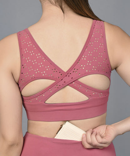 A woman wearing the Peony Pink Netted Top with a cutout back is placing a cardholder into her waistband pocket.