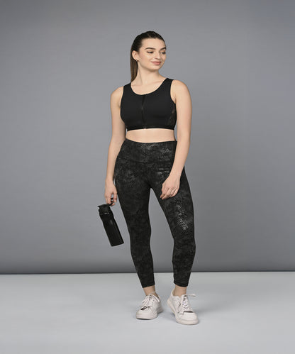 Woman wearing the Zipped Sports Bra & Metallic Legging activewear set, holding a water bottle and smiling while standing against a plain gray background.