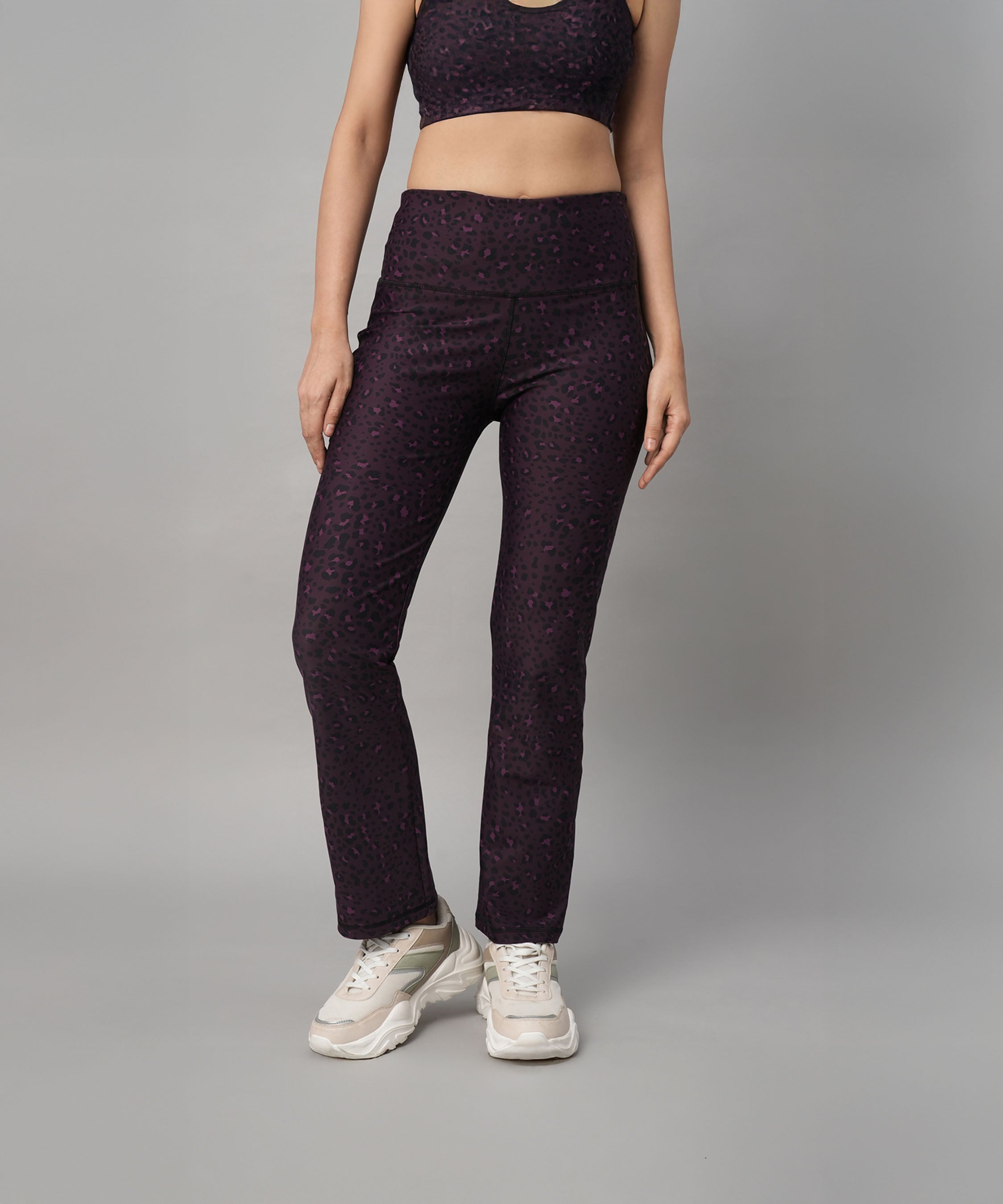Woman in stylish Pink Animal Print Wide Legged Leggings paired with a matching activewear top and white sneakers, standing against a gray background.
