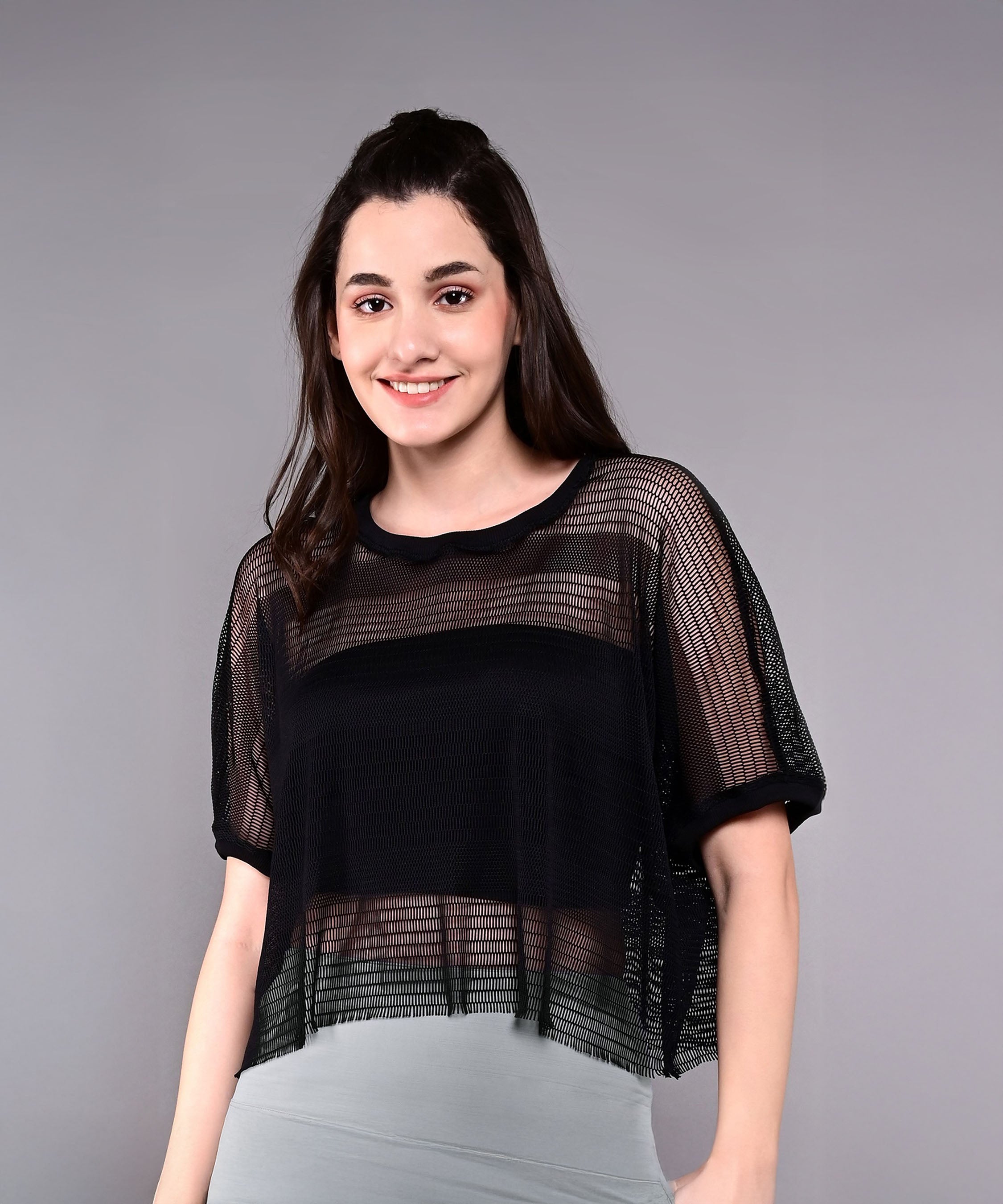 A woman smiles while wearing the Tuna Active Black Netted Top over a light grey outfit, standing against a plain grey background.