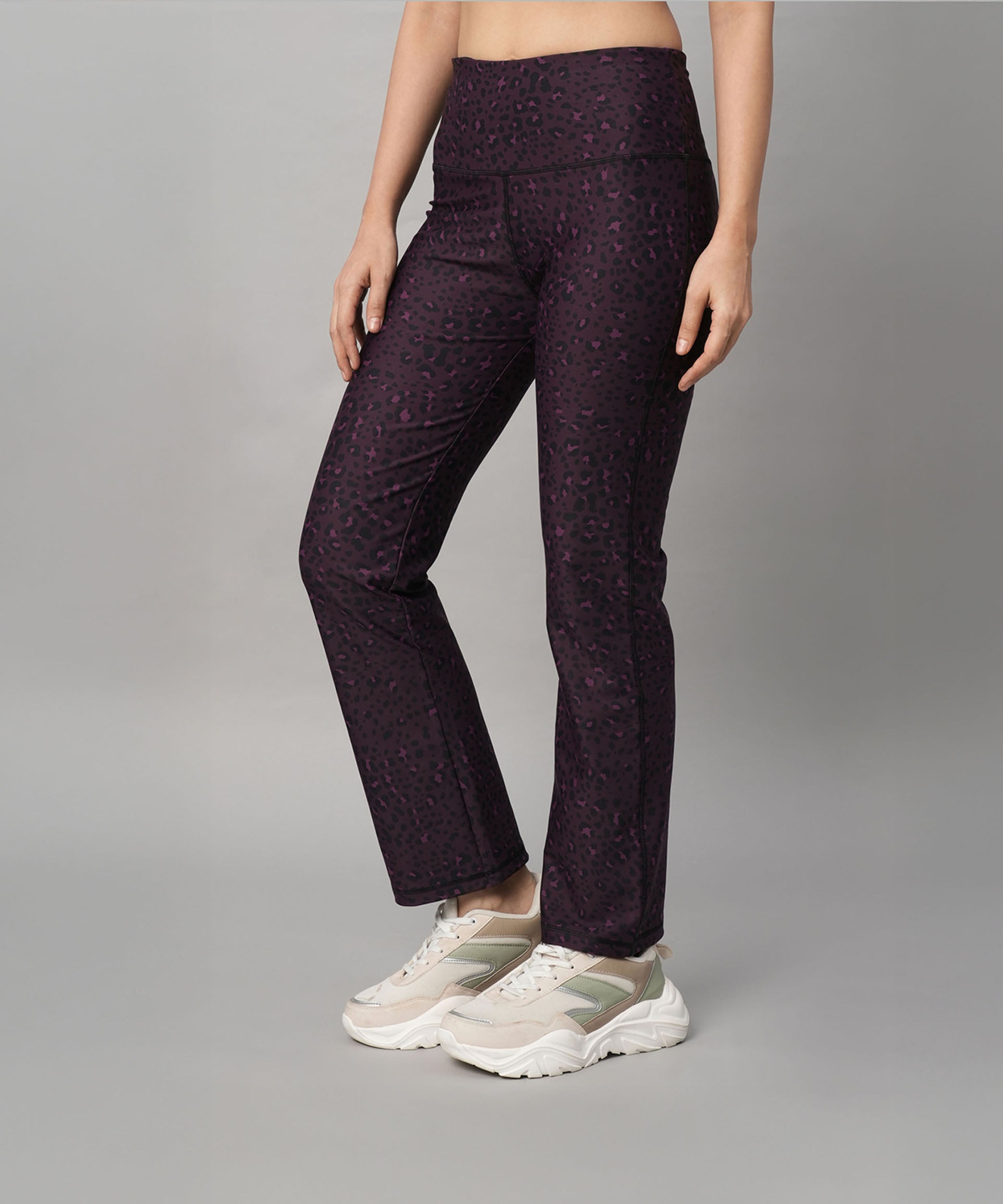 Woman wearing Pink Animal Print Wide Legged Leggings and white sneakers, standing against a gray background.
