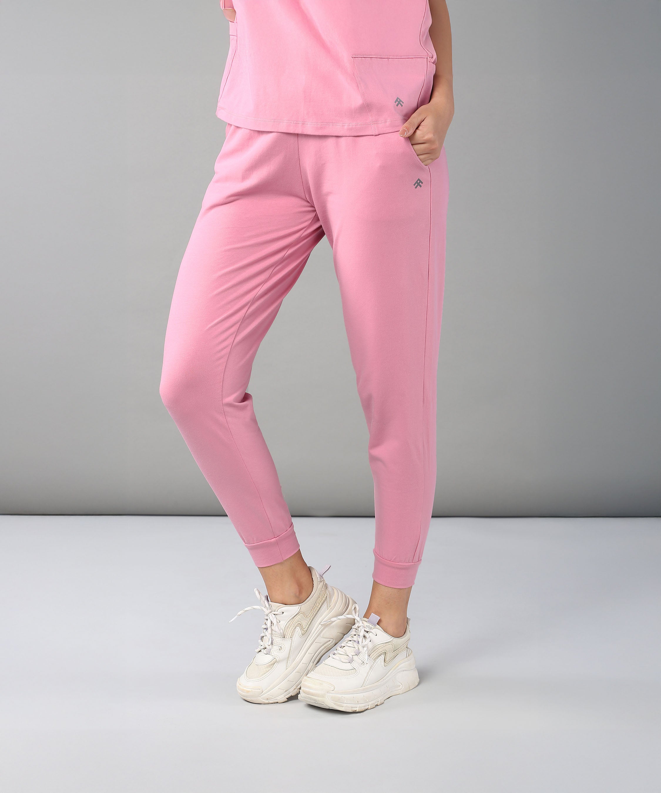 Person dressed in the Flamingo Pink Chic Ensemble—featuring buttery soft Joggers Cotton Lycra and a matching Racer Back top—paired with white sneakers, stands against a plain gray background.
