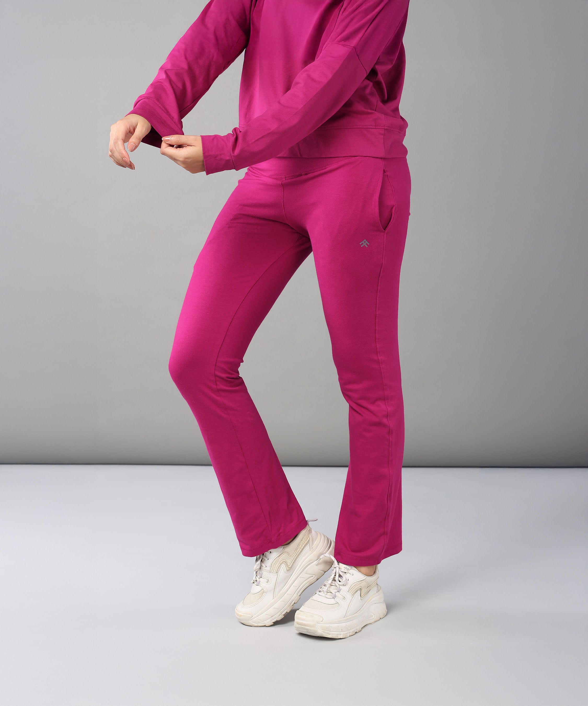 Wearing the Deep Pink Comfort Duo—cotton lycra joggers and top—paired with white sneakers, this person stands against a plain background.
