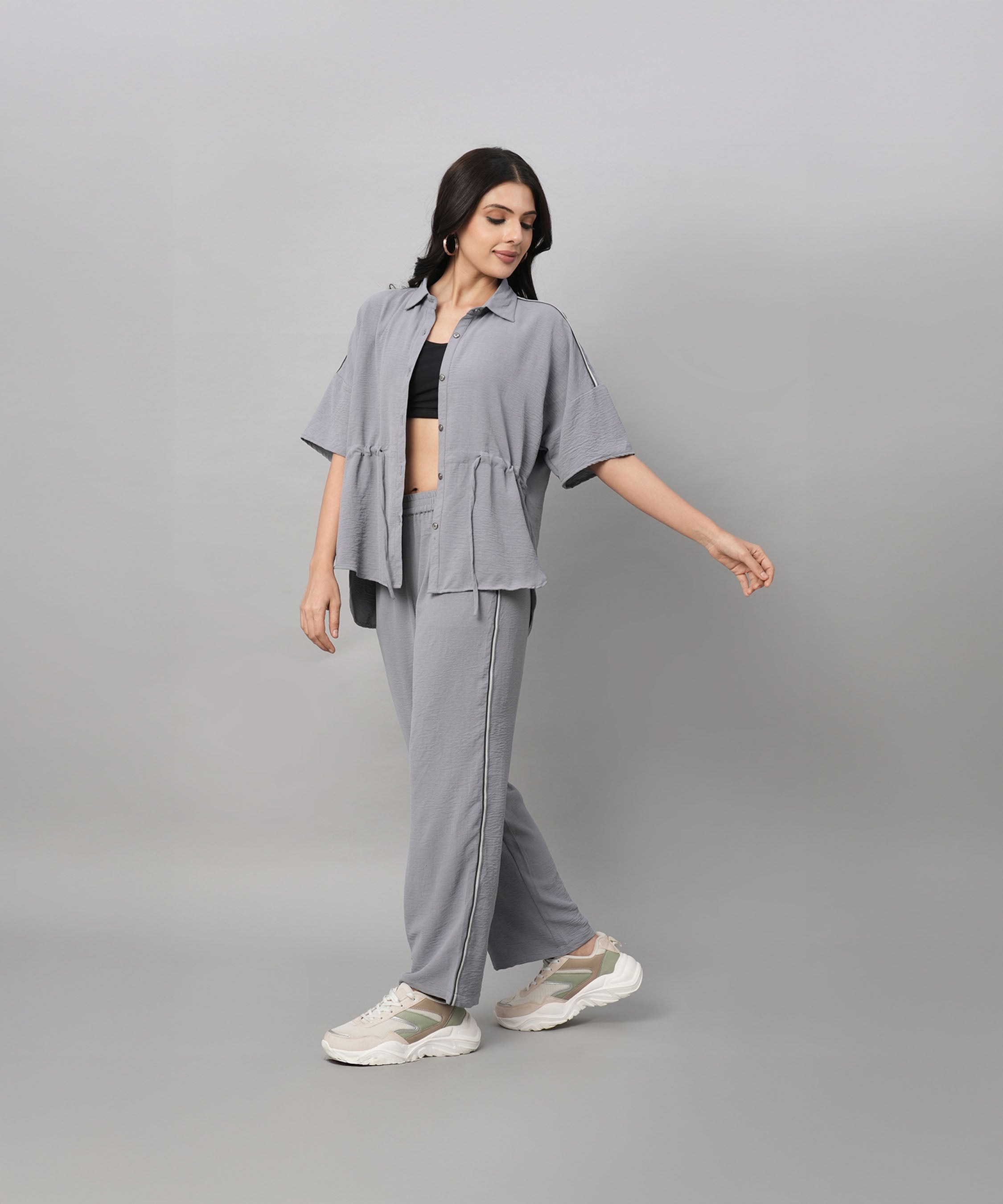A woman wearing the Grey Tie Up Top with Loose Pants Cord Set and sneakers poses against a plain light gray background.
