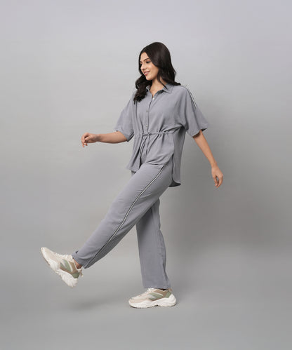 A woman wears the Grey Tie Up Top with Loose Pants Cord Set, pairing the coordinated grey outfit with white sneakers as she walks against a plain grey background.